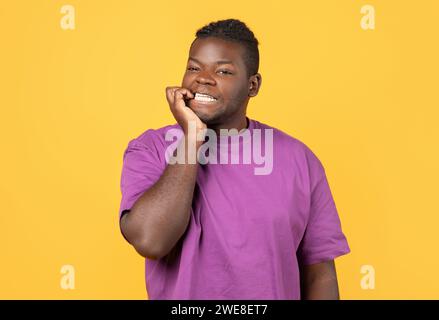 Ragazzo afro-americano che esprime ansia mordere le unghie su sfondo giallo Foto Stock