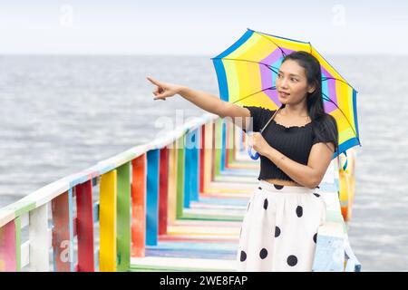 Una giovane donna con un ombrellone si trova sulla passerella colorata e punta con la mano Foto Stock