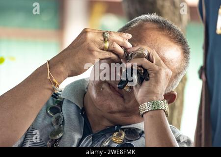 AYUTTHAYA, THAILANDIA, 10 dicembre 2023, Un uomo con una lente d'ingrandimento esamina i gioielli per strada Foto Stock