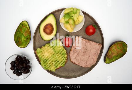 Colazione con paté di foie gras e avocado su pane tostato con olive nere a parte, isolato su sfondo bianco Foto Stock