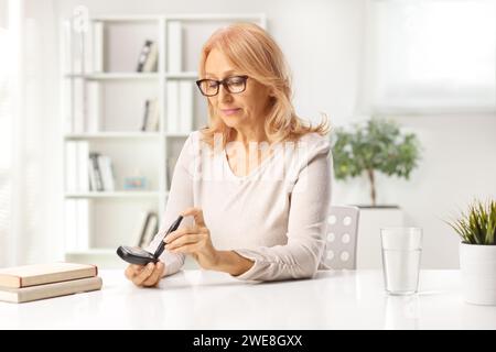 Donna di mezza età con monitor del glucosio che controlla il livello di insulina a casa Foto Stock