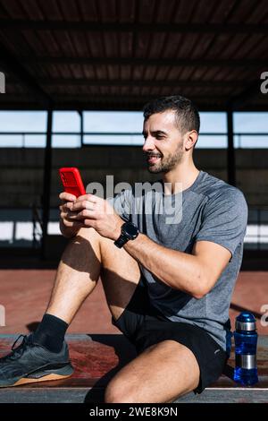 Mettiti in forma con lo smartphone rilassati riposando dopo l'esercizio in una panchina all'aperto. L'atleta sportivo attivo invia SMS al telefono durante l'allenamento. Foto Stock