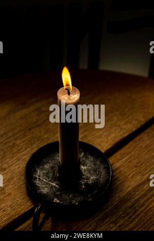 Alto angolo di bruciatura e illuminazione della candela di cera nel vassoio dell'impugnatura mentre è posizionato su un tavolo di legno con crepe in una stanza buia Foto Stock