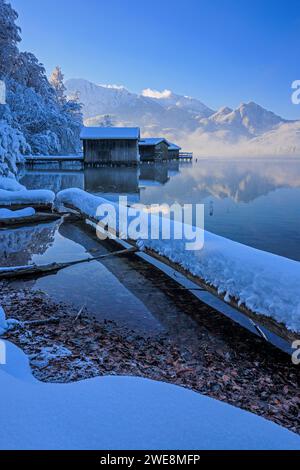 Boathouses, riflesso delle montagne nel lago, inverno, neve, sole, Lago Kochelsee, alta Baviera, Baviera, Germania, Europa Foto Stock