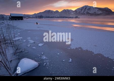 Rossore mattutino sul lago ghiacciato di fronte alle montagne, lago Kochelsee, alta Baviera, Baviera, Germania, Europa Foto Stock