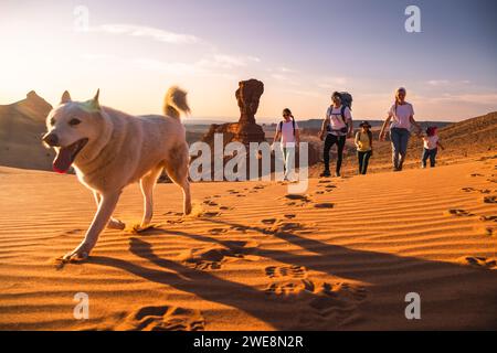 Padre di famiglia, madre e figlie piccole camminano con un cane bianco nel deserto del Gobi Foto Stock