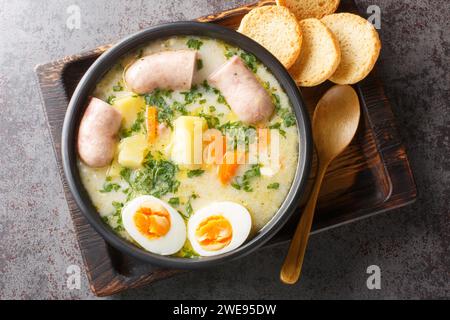 Zuppa tradizionale polacca Zurek su pasta madre di segale con salsiccia e uova da vicino in una ciotola sul tavolo. Vista superiore orizzontale dall'alto Foto Stock