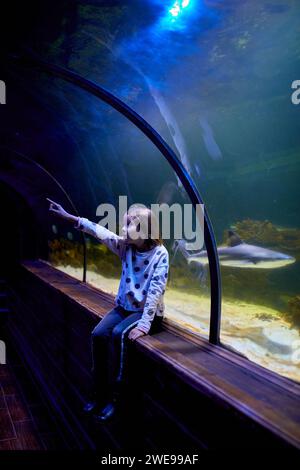 Una giovane ragazza deliziosa guarda con stupore gli squali scivolare sopra il tunnel trasparente dell'oceanarium. Foto Stock