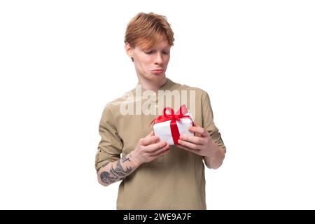 un giovane ragazzo dai capelli rossi con gli occhiali e una camicia marrone decide chi regalare una confezione regalo con una sorpresa Foto Stock