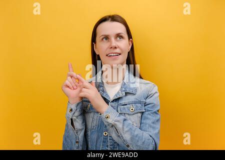 Ritratto di bella e premurosa giovane donna che piega le dita, conta e guarda con contemplazione, calcolo, indossa una giacca in denim, posa isola Foto Stock