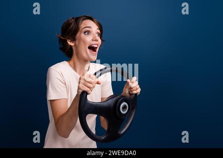 Ritratto fotografico di una giovane donna attraente che guida un timone eccitato, vestita con eleganti abiti bianchi isolati su sfondo blu scuro Foto Stock