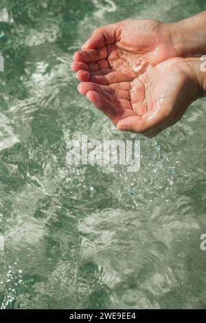 Mani con acqua pura. Tenere l'acqua in mani chiuse. Primo piano della mano di una donna che tocca l'acqua del lago. La mano di una persona che si allunga per toccare un rippl Foto Stock