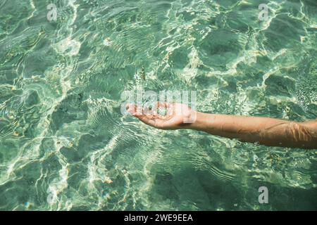 Mani con acqua pura. Primo piano della mano di una donna che tocca l'acqua del lago. La mano di una persona che si allunga per toccare una superficie d'acqua che si ripete, esplorando la Foto Stock