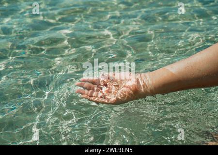 Mani con acqua pura. Primo piano della mano di una donna che tocca l'acqua del lago. La mano di una persona che si allunga per toccare una superficie d'acqua che si ripete, esplorando la Foto Stock