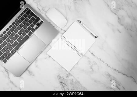 Vista dall'alto di un computer portatile grigio su sfondo in marmo bianco. Blocco appunti, mouse e penna, spazio per la copia. Foto Stock