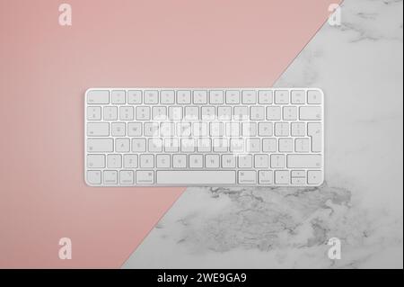 Vista dall'alto della tastiera bianca su sfondo in marmo rosa e bianco. Moderno spazio per fotocopie e ufficio. Foto Stock