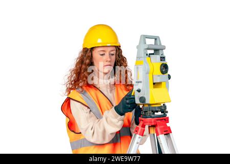 Donna rossa con elmetto giallo e topografo ppe giallo che lavora con il moderno tachimetro con strumenti geodetici per il controllo delle coordinate. Giovane Wom Foto Stock