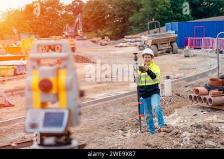 Felice geometri donna che lavora con apparecchiature per elettroerosione a stazione totale teodolite in un cantiere edile all'aperto Foto Stock