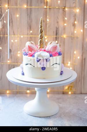 Torta unicorno con corno fondente dorato, ciglia e formaggio cremoso glassa su sfondo festoso bokeh Foto Stock