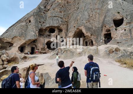 Turisti che visitano le antiche abitazioni nelle grotte in un paesaggio roccioso, in Cappadocia, Turchia, con una guida che ti indicherà i dettagli. Foto Stock