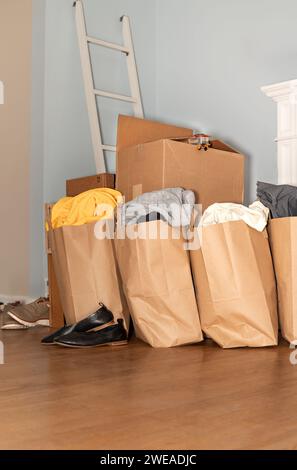 Scatole di cartone con vestiti, scarpe sul pavimento oggetti e oggetti per muoversi, traslocare il giorno e muoversi. Foto verticale con spazio per la copia. Foto Stock