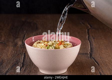 Versare acqua calda su spaghetti istantanei secchi con ingredienti secchi e spezie. Copia spazio. Foto Stock