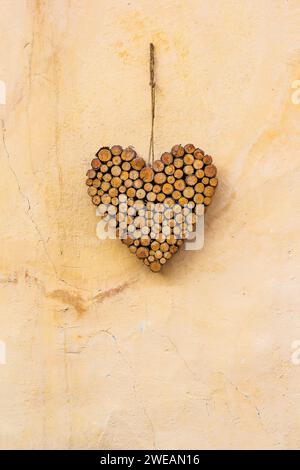 Decorazione a forma di cuore realizzata con piccoli bastoncini di legno appesi alla parete gialla come sospiro di benvenuto Foto Stock