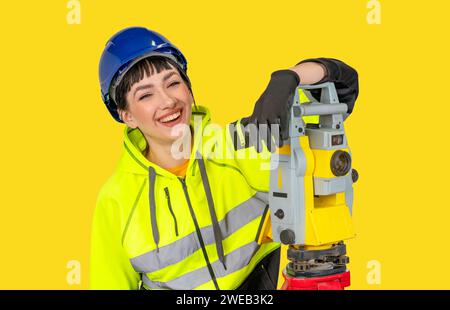 Donna sorridente con elmetto e indumenti protettivi topografo che lavora con strumenti geodetici moderni tachimetro che controlla le coordinate. Voi Foto Stock