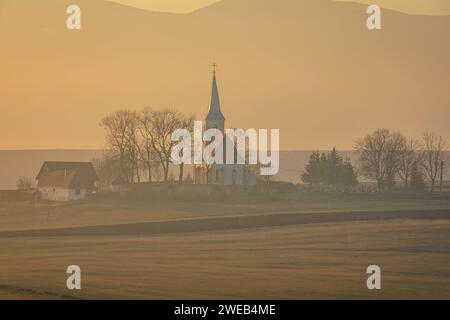 La vecchia chiesa di Delnita durante un tramonto spettacolare. Foto aerea scattata il 29 dicembre 2023 a Delnita, contea di Harghita, Transilvania, Romania. Foto Stock