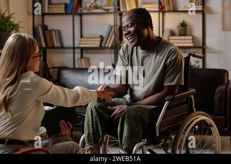 Veterano nero gioioso con disabilità che stringe la mano della sua terapista femminile dopo una sessione di successo Foto Stock