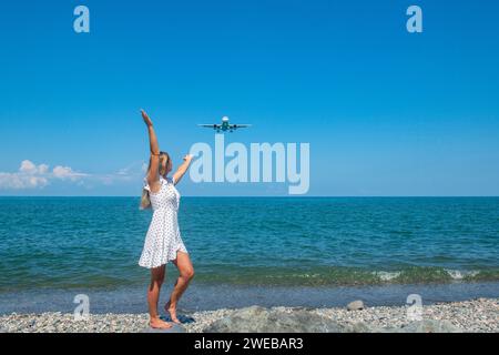 Skybound Connection: La ragazza in abito bianco incontra un aereo sopra il Mar Blu Foto Stock