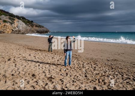 Due donne in piedi su una spiaggia, che fanno lo stesso gesto per proteggere gli occhi dalla luce del sole. Giovani madre e figlia proteggono i loro occhi. Foto Stock