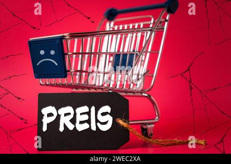 24 gennaio 2024: Carrello con smiley negativo triste, sfondo sgretolante ed etichetta con la scritta: Price FOTOMONTAGE *** Einkaufswagen mit einem traurigen negativen Smiley, bröckelnden Hintergrund und und einem Etikett mit Aufschrift: Preis FOTOMONTAGE Foto Stock