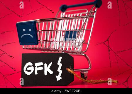 24 gennaio 2024: Carrello della spesa con un sorriso triste, sfondo sgretolante e un'etichetta con la scritta: GFK consumer climate index shows negative consumer sentiment FOTOMONTAGE *** Einkaufswagen mit einem traurigen Smiley, bröckelnden Hintergrund und einem Etikett mit Aufschrift: GFK Konsumklimaindex zeigt negative Verbrauchermung FOTOMONTAGE Foto Stock