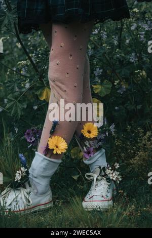 Personaggi stravaganti - sorelle che si tengono per mano e che si divertono con fiori luminosi nei loro panni - che piantano bambini nella natura per crescere. Foto Stock