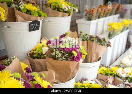 Negozio di fiori freschi che espone crisantemi e altri all'interno di vasi o vasi bianchi. Foto Stock