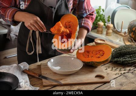 Donna che rimuove i semi dalla zucca cruda al tavolo di legno in cucina, primo piano Foto Stock