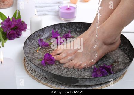 Donna che versa acqua sui piedi in una ciotola sul pavimento bianco, primo piano. Trattamento spa Foto Stock