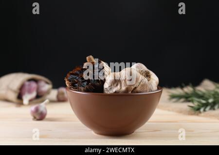 Bulbi di aglio nero fermentato in ciotola su tavolo di legno Foto Stock