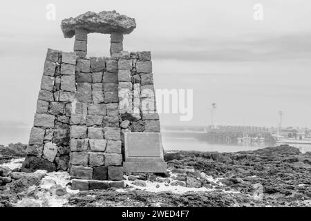 Antico faro bianco e nero realizzato con pietre a taglio quadrato sulla costa di un piccolo porto sull'isola di Jeju, Corea del Sud Foto Stock