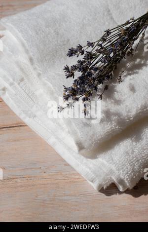 Fiori di lavanda accanto a un asciugamano di cotone bianco su sfondo di legno. Aromaterapia e concetto biologico. Natura morta delle erbe di lavanda essiccate. Concetto ecosostenibile Foto Stock
