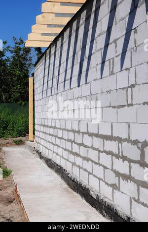 Impermeabilizzazione del seminterrato: Un primo piano della fondazione di una casa, impermeabilizzazione esterna del seminterrato all'esterno della casa in costruzione con una passerella in cemento Foto Stock