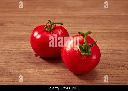 Due pomodori freschi con steli verdi sono collocati su uno sfondo rustico di legno. Il pomodoro porta molti benefici per la salute, alto contenuto nutrizionale e h Foto Stock