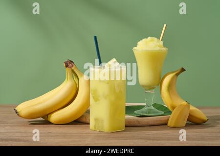 Concetto per pubblicizzare prodotti con ingredienti di banana. Banane mature e bicchieri di succo e frullato alla banana su un tavolo di legno. Le banane sono una delle th Foto Stock