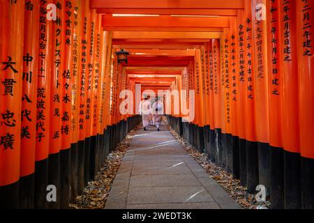 Le donne in kimono tradizionale giapponese camminano attraverso le porte rosse torii del santuario Fushimi Inari a Kyoto, in Giappone. Foto Stock