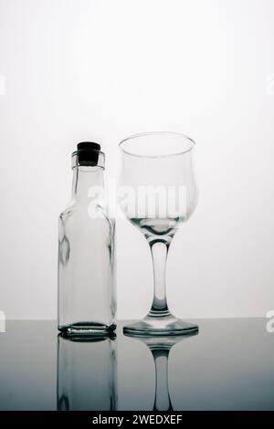 Bottiglia in vetro trasparente con bicchiere di vino vuoto su sfondo bianco Foto Stock