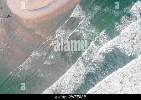 Un colpo aereo delle schiumose onde dell'oceano che colpiscono la spiaggia sabbiosa Foto Stock