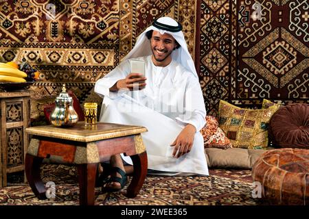 Uomo degli emirati che indossa un abito kandura trascorre del tempo in una casa tradizionale araba a Dubai Foto Stock
