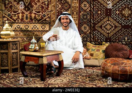 Uomo degli emirati che indossa un abito kandura trascorre del tempo in una casa tradizionale araba a Dubai Foto Stock