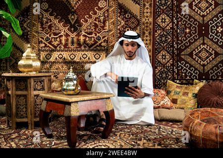 Uomo degli emirati che indossa un abito kandura trascorre del tempo in una casa tradizionale araba a Dubai Foto Stock